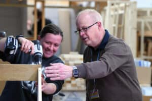 A female carpentry learner with carpentry tutor demonstrating a skill.