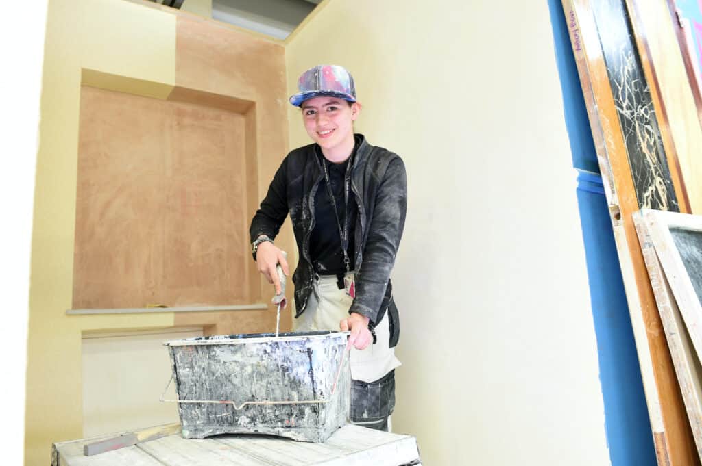 Female painting and decorating learner using a roller to paint a wall.