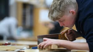A carpentry learner cutting wood with a hand saw