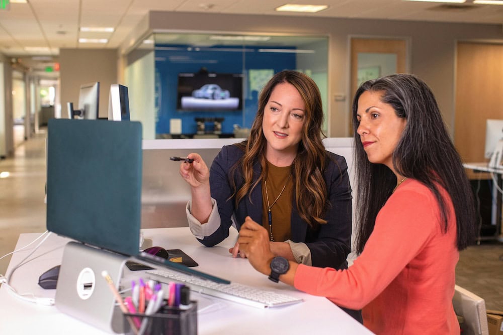 Two women working on a computer in an office.