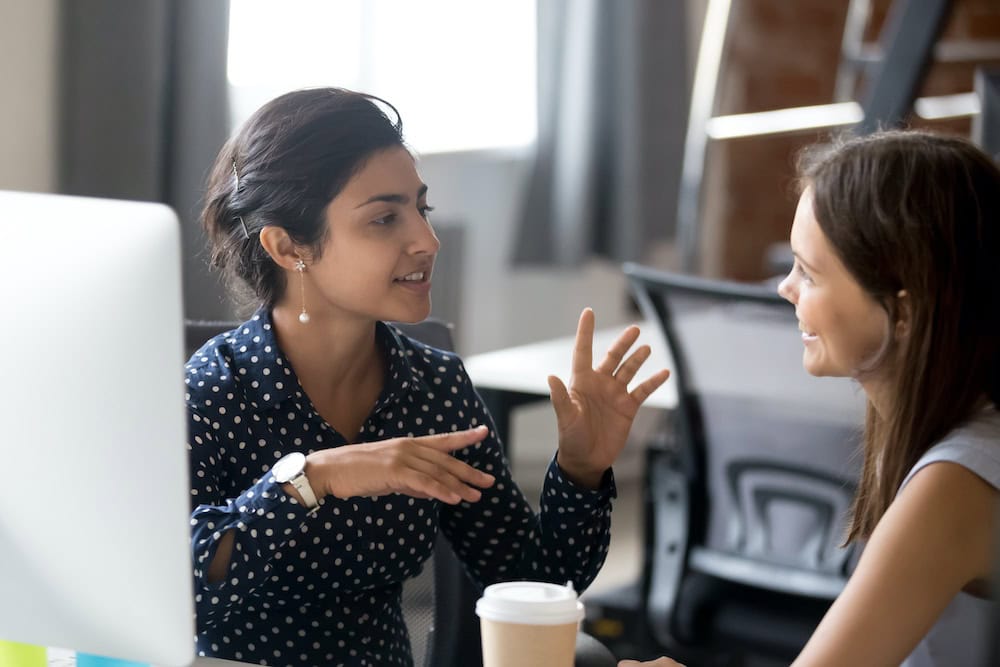 Two women talking in an office setting.