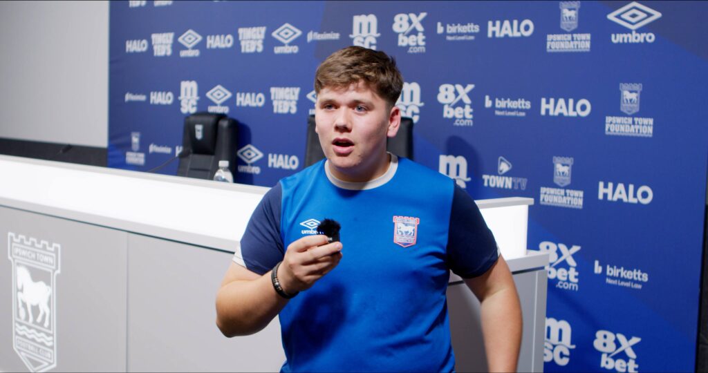 Young male football player in Ipswich Town FC kit speaking at press conference at Suffolk New College.