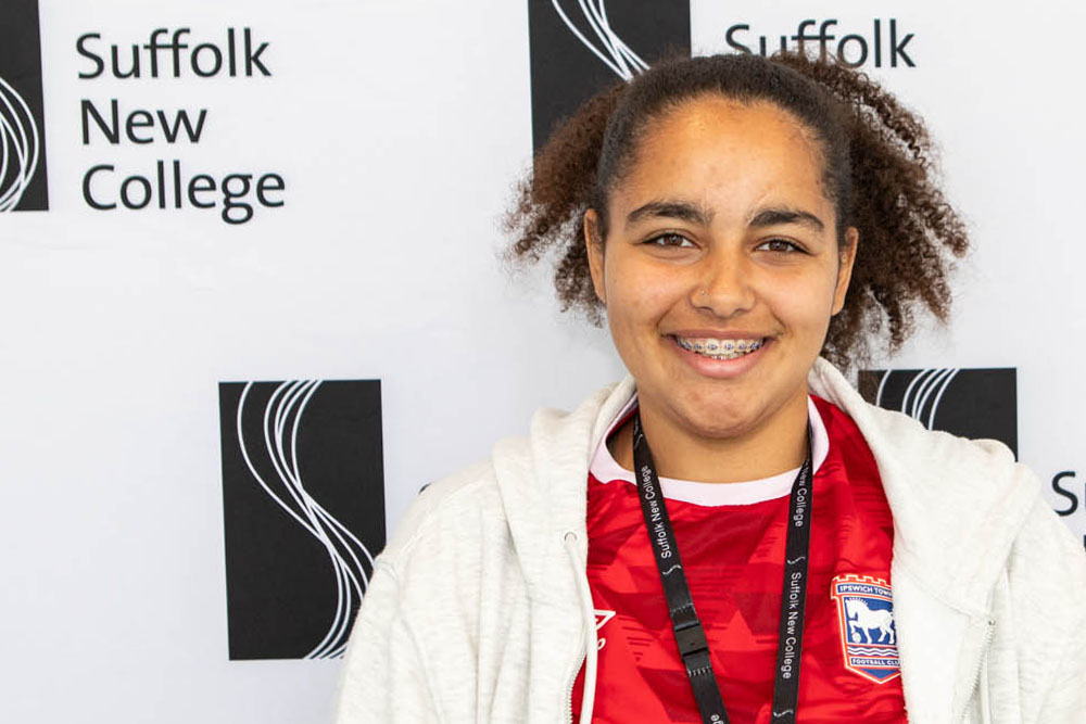 Student wearing Ipswich Town FC jersey at Suffolk New College campus in front of college signage.