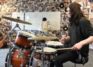 Learner plays the drums whilst another learner makes notes on a whiteboard