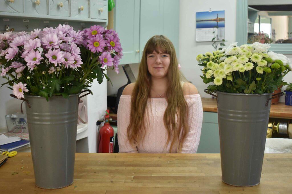 Vibrant pink and white flowers in grey metal buckets on a wooden table in Suffolk New College floral workshop.