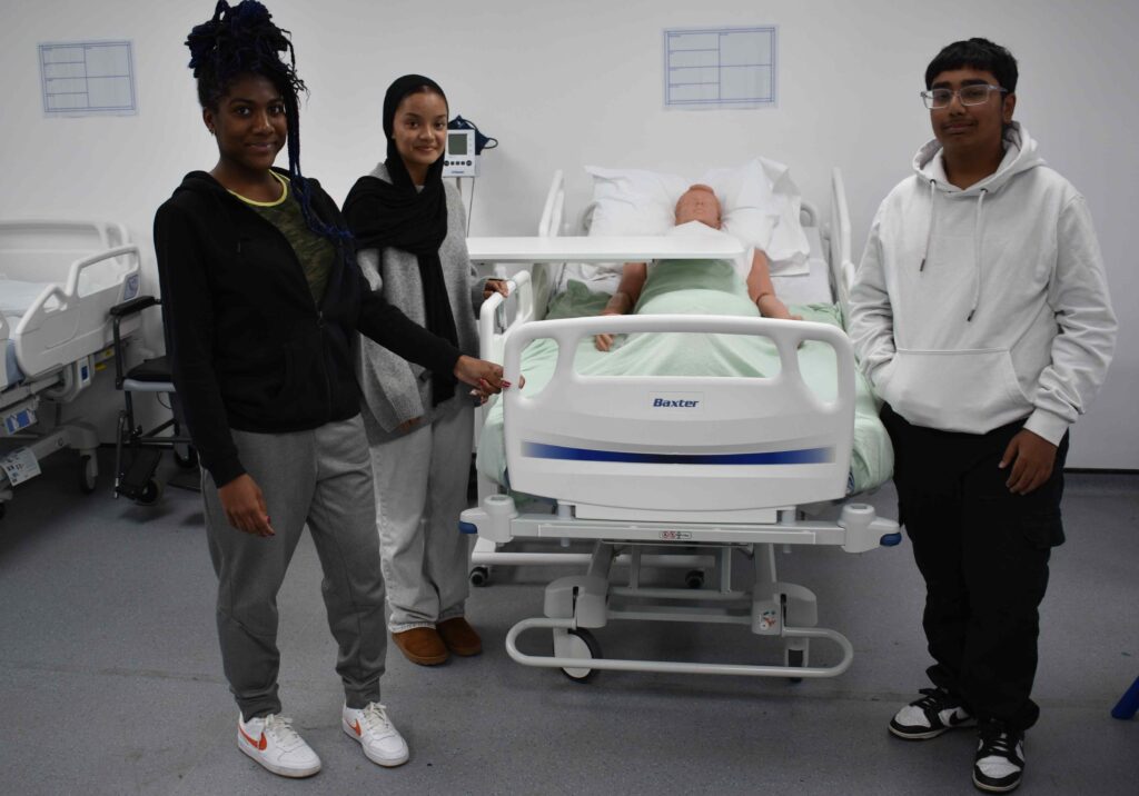 Students practicing healthcare skills on a hospital bed at Suffolk New College healthcare training facilities, demonstrating nursing and medical simulations for student learning.