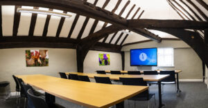 Modern classroom at Suffolk New College with exposed wooden beams, large screen, and colourful flower artwork, ideal for visual arts or digital media courses.