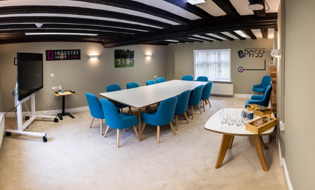 Modern training room at Suffolk New College with large table, blue chairs, and technology setup for student and staff meetings.