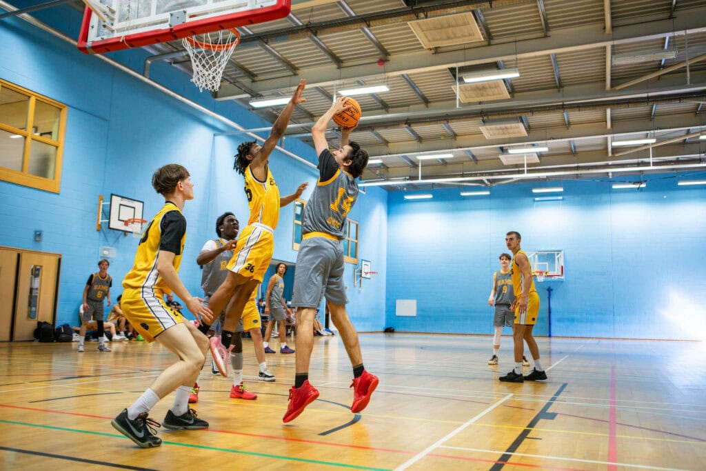 Energetic basketball students practicing in Suffolk New College sports hall for sports and fitness training.College basketball players competing in indoor gymnasium at Suffolk New College sports facilities.