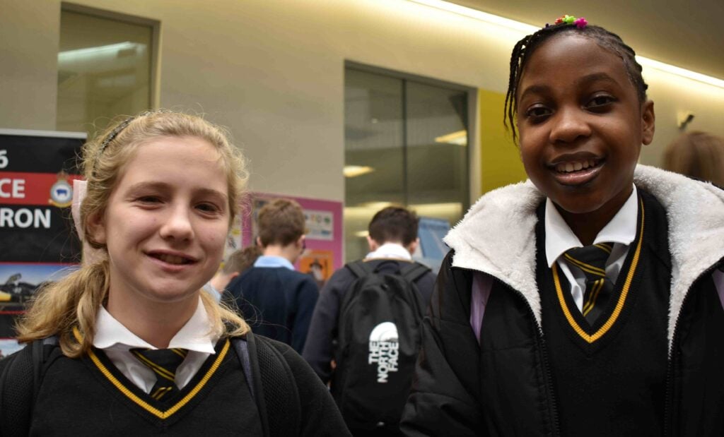 Diverse group of secondary school students at Suffolk New College campus, smiling and engaged, wearing school uniforms, in an educational environment focused on student success and development.