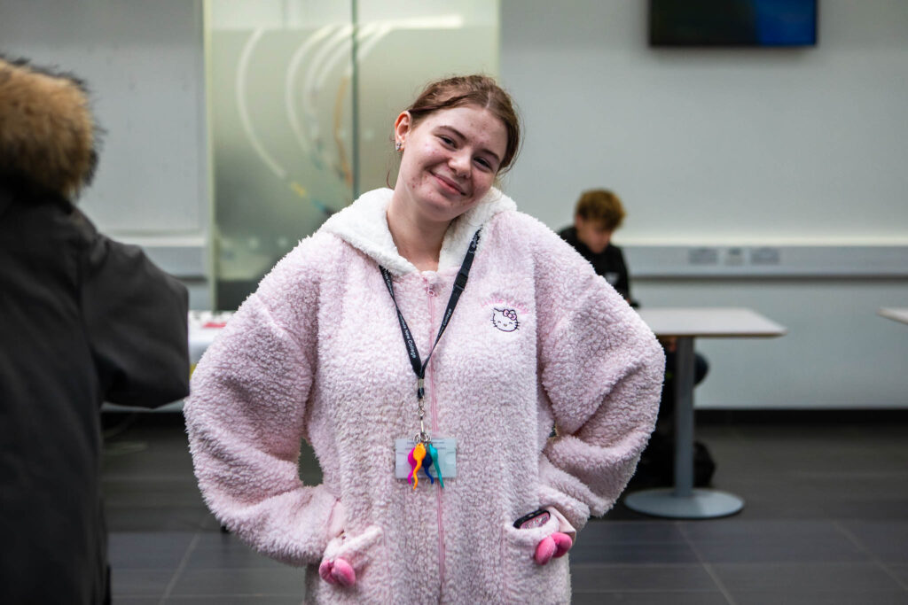 Bright young student smiling inside Suffolk New College classroom, wearing a cosy hoodie and college ID badge, engaging in a friendly educational environment.