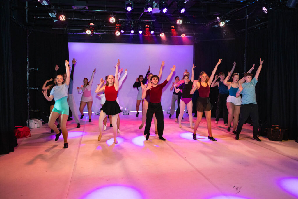 Diverse group of students performing dance routines on stage at Suffolk New College, highlighting arts and performing arts education.