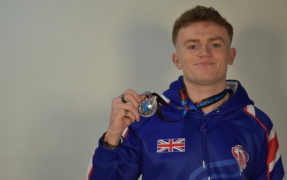 Young male athlete displaying medal at Suffolk New College sports facility.