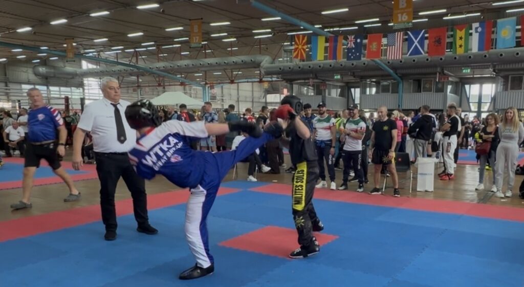 A martial arts competition at Suffolk New College showcasing students in a combat sport environment with spectators and flags from different countries.