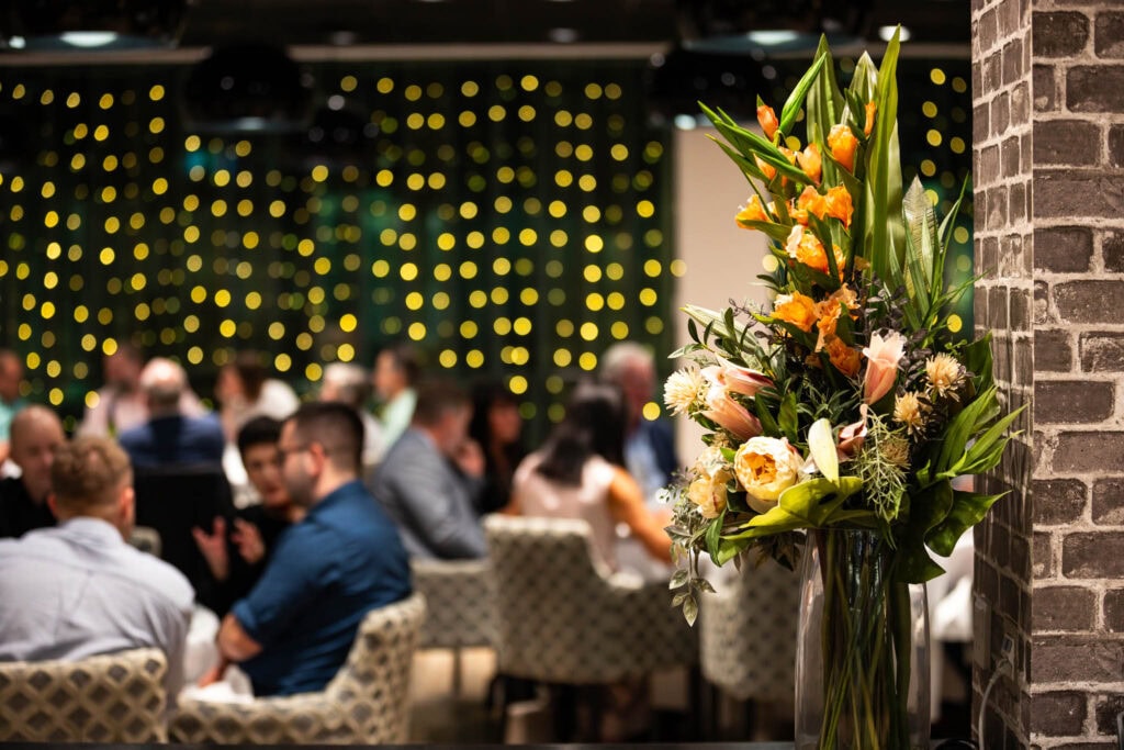 Vibrant flower arrangement in a glass vase at Suffolk New College event, with guests socialising and the ambiance of the college's engaging environment and student activities.