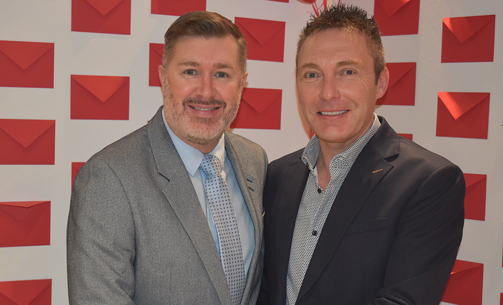 Two men in suits smiling at Suffolk New College Valentine's themed event, celebrating apprenticeships and industry partnerships with a festive backdrop.