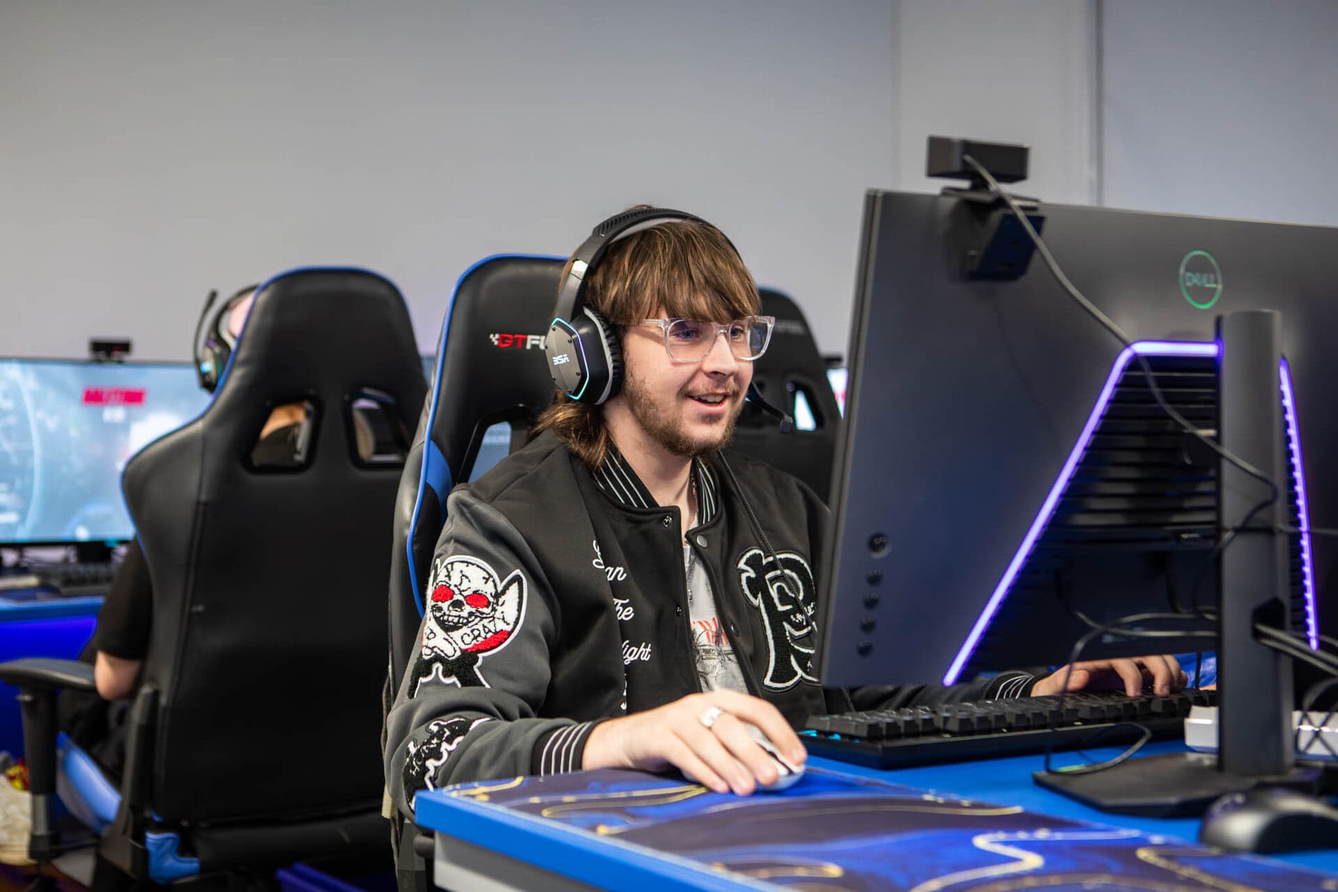 Student in Suffolk New College's Information Technology class working on a computer with gaming headset in a modern classroom setting.