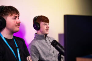 Two students working on information technology projects at Suffolk New College, engaging in practical learning with computers and headphones in a classroom setting.