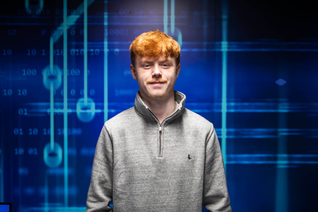 A young male esports student at Suffolk New College standing in front of a digital background with binary code and data graphics, highlighting gaming and digital skills development.