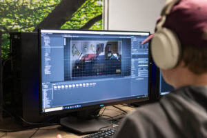 Student wearing headphones working on game design project on dual monitors at Suffolk New College, focusing on game development and digital creativity.