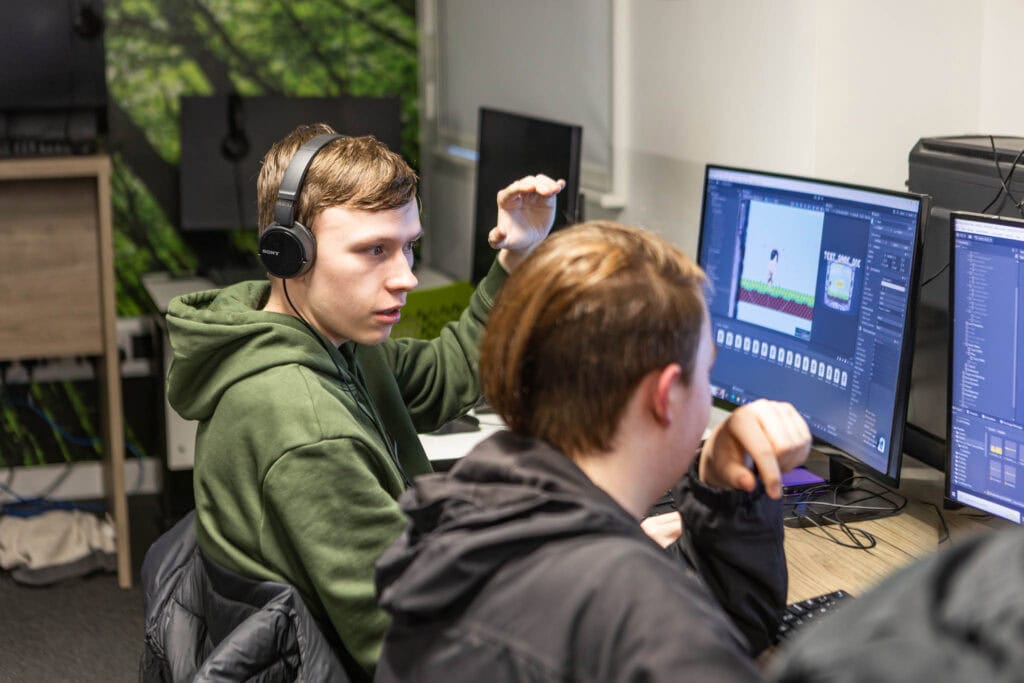 Two students working on game design projects at Suffolk New College, using computers with game development software, in a classroom setting.