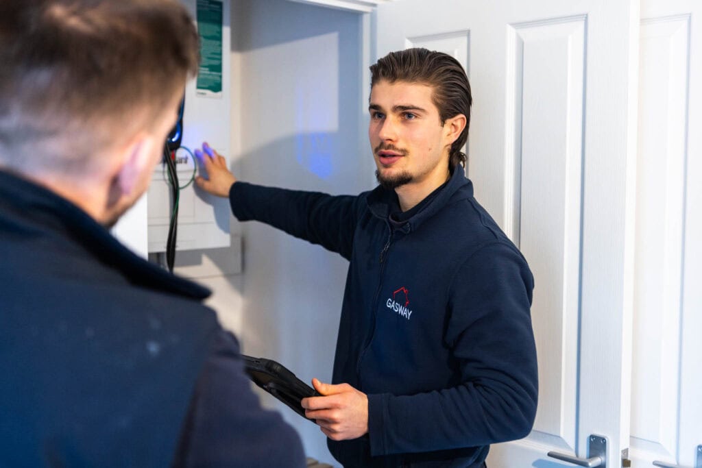 Young man in Suffolk New College uniform providing technical training to an apprentice, demonstrating practical skills in a classroom setting.