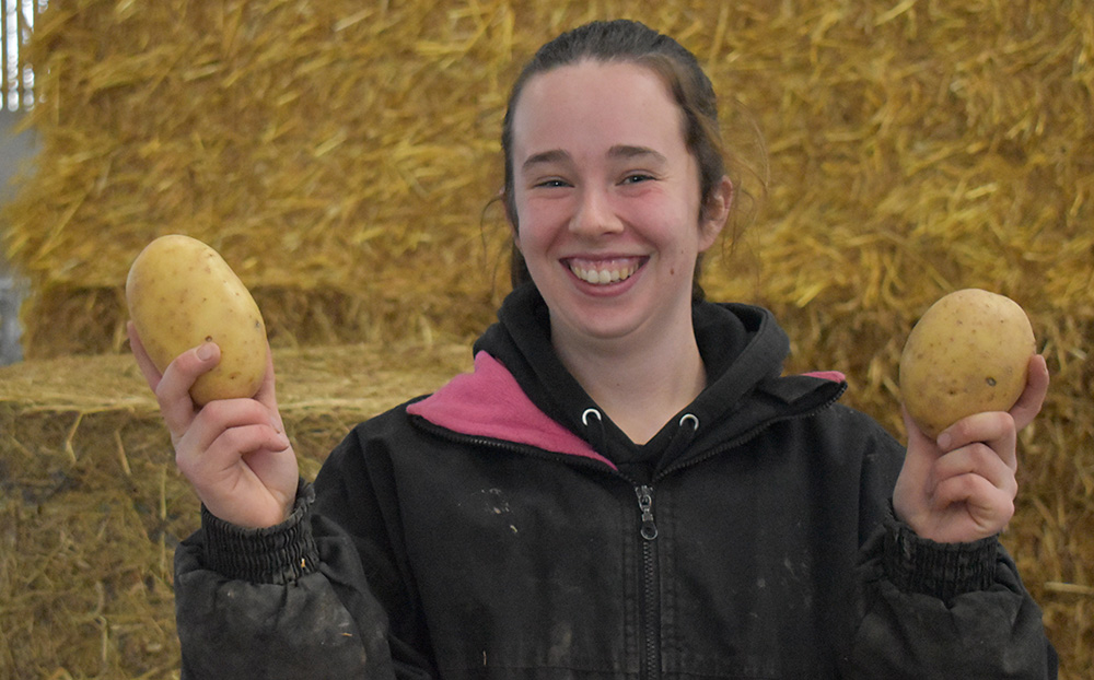 A young woman holding two large potatoes at Suffolk New College during the East Anglia spud celebration day, showcasing agricultural skills and potato farming expertise.