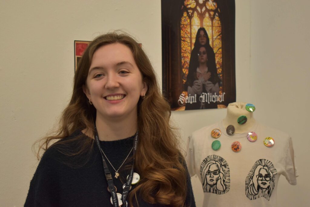 A smiling young woman with long brown hair standing in front of an art display at Suffolk New College, showcasing her passion for the arts before university.