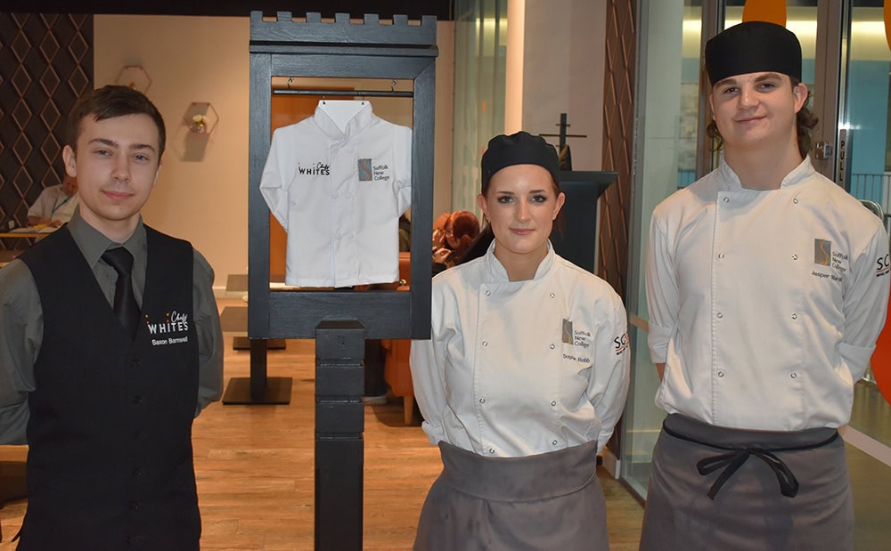 Three Suffolk New College students in chef uniforms standing indoors, showcasing culinary skills and education in a professional environment.