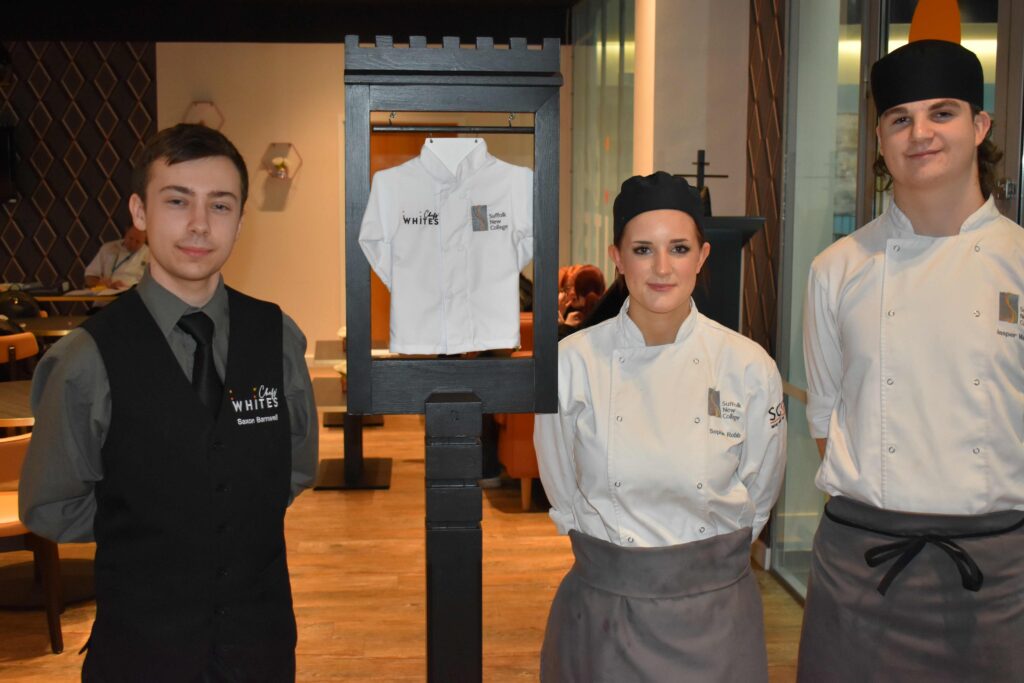 Three Suffolk New College students in chef uniforms standing in a restaurant, preparing for a national restaurant competition, showcasing their culinary skills and teamwork.