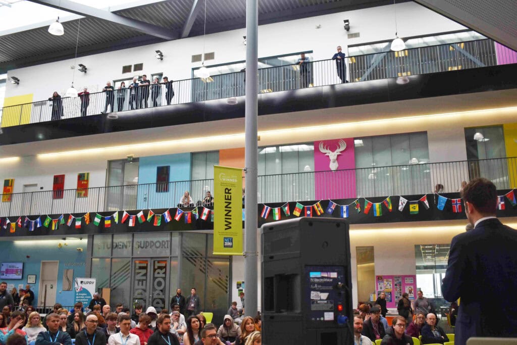 Students and staff at Suffolk New College in Ipswich attending a cultural event, with multiple floors, banners, and a diverse group of attendees celebrating local culture.
