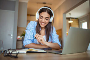 Smiling woman with headphones studying online at home, representing adult courses and flexible learning options at Suffolk New College.