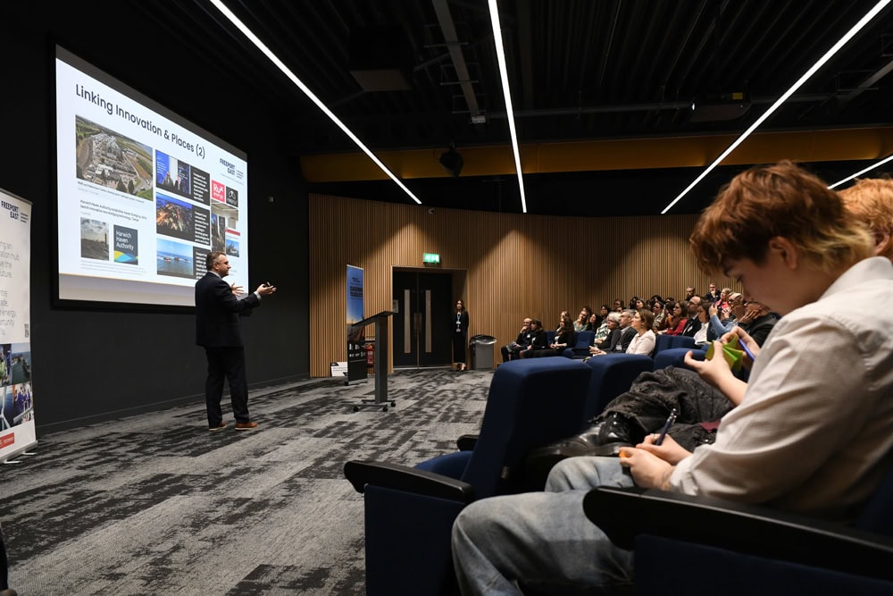A speaker presenting on linking innovation and success at Suffolk New College, with an engaged audience attending a business and education event.