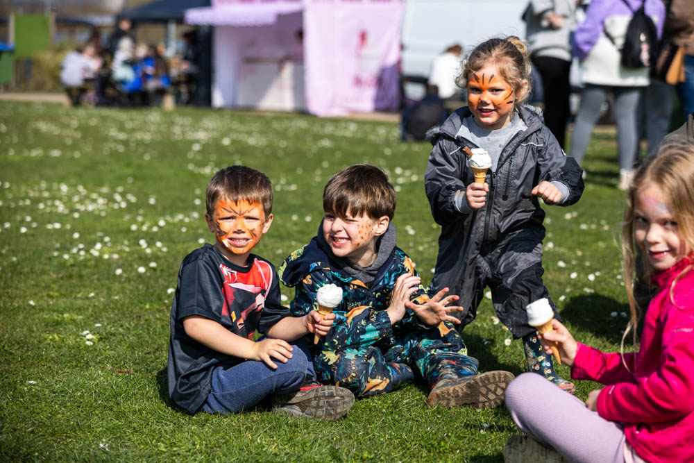 Children enjoying a spring family fun day at Suffolk New College, with face paint, ice cream, and outdoor activities on a sunny day.