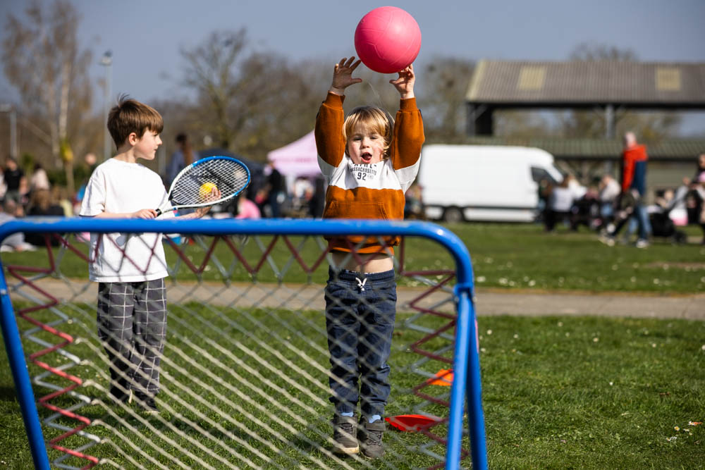 Children enjoying a spring family fun day at Suffolk New College, with kids playing with a pink ball and tennis rackets outdoors on a sunny day.