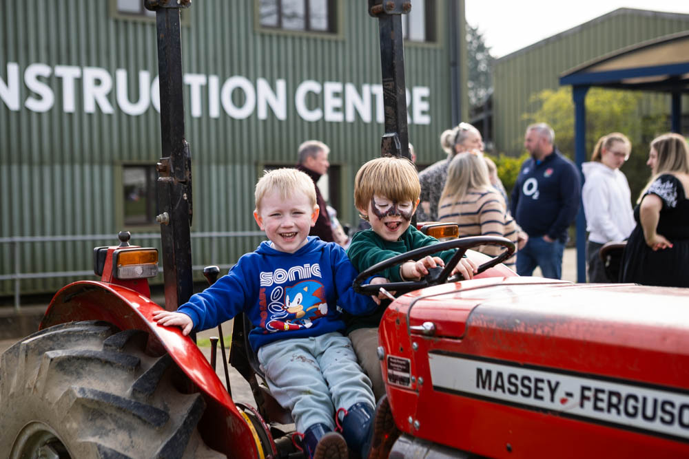 Two children enjoying a tractor ride at Suffolk New College's spring family fun day, part of the 'lambtastic' event attracting families and visitors to the college.