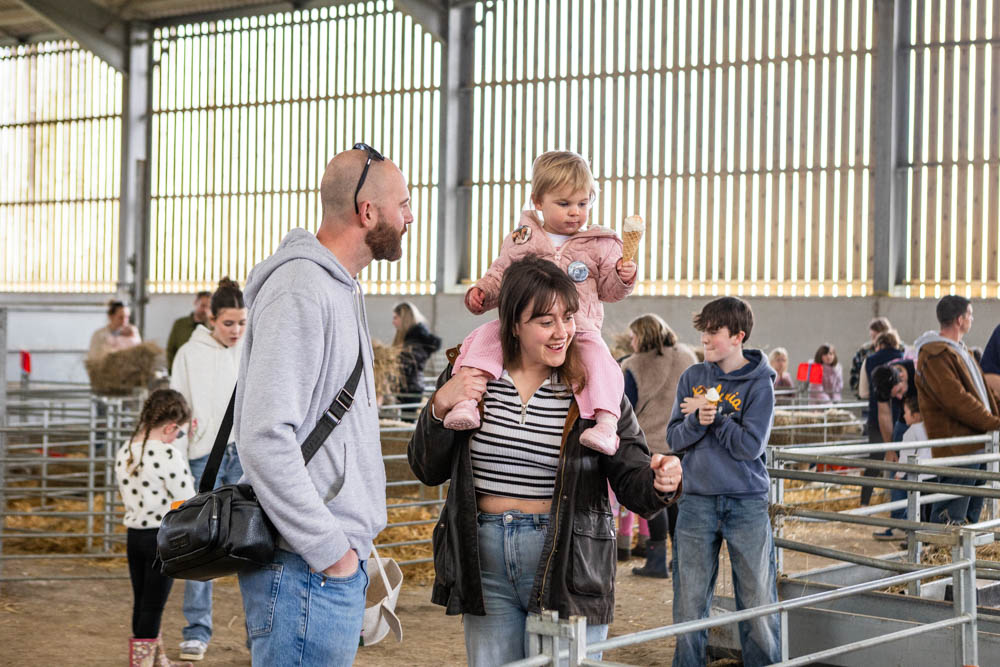 Families enjoying the 'lambtastic' spring fun day at Suffolk New College, with children and adults exploring farm animals and activities in a large indoor barn setting.