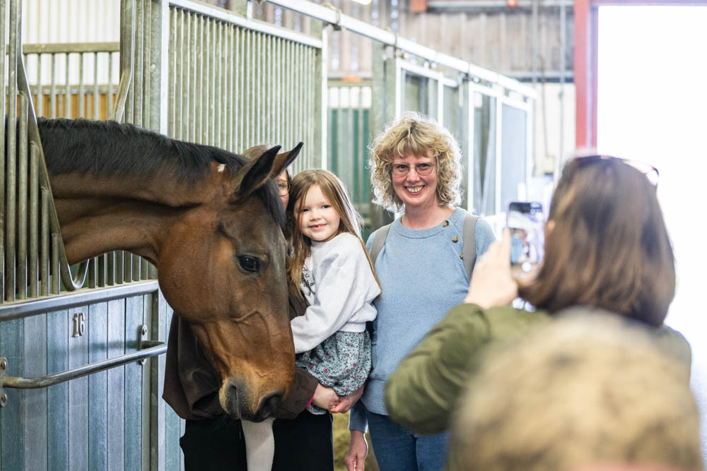 Family enjoying a spring day at Suffolk New College, with children petting a horse and taking photos during the 'lambtastic' family fun event.