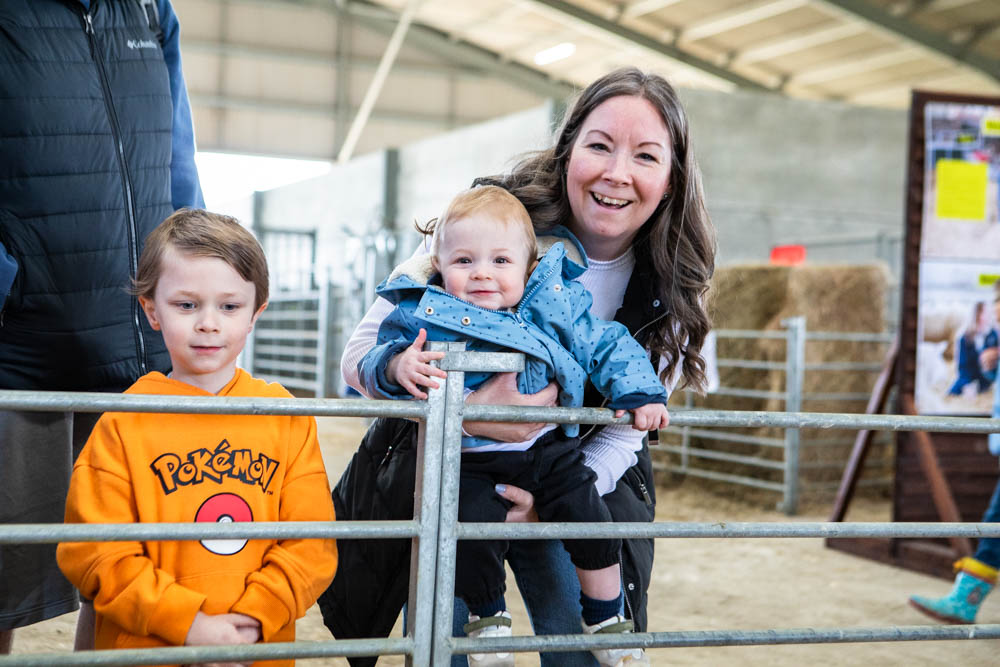 A woman with two children enjoying a spring family fun day at Suffolk New College, with animals and activities in the background, attracting families and children.