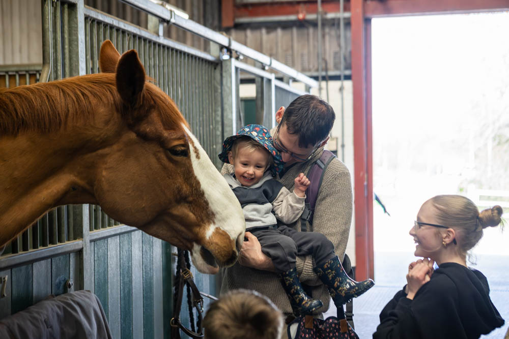 Family enjoying a lambtastic spring day at Suffolk New College, with children and adults interacting with a friendly horse during the college's family fun event.