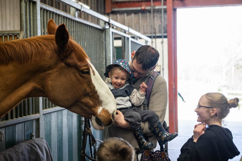 A father and young girl enjoy a close-up encounter with a brown horse at Suffolk New College's spring family fun day, attracting many visitors and families.