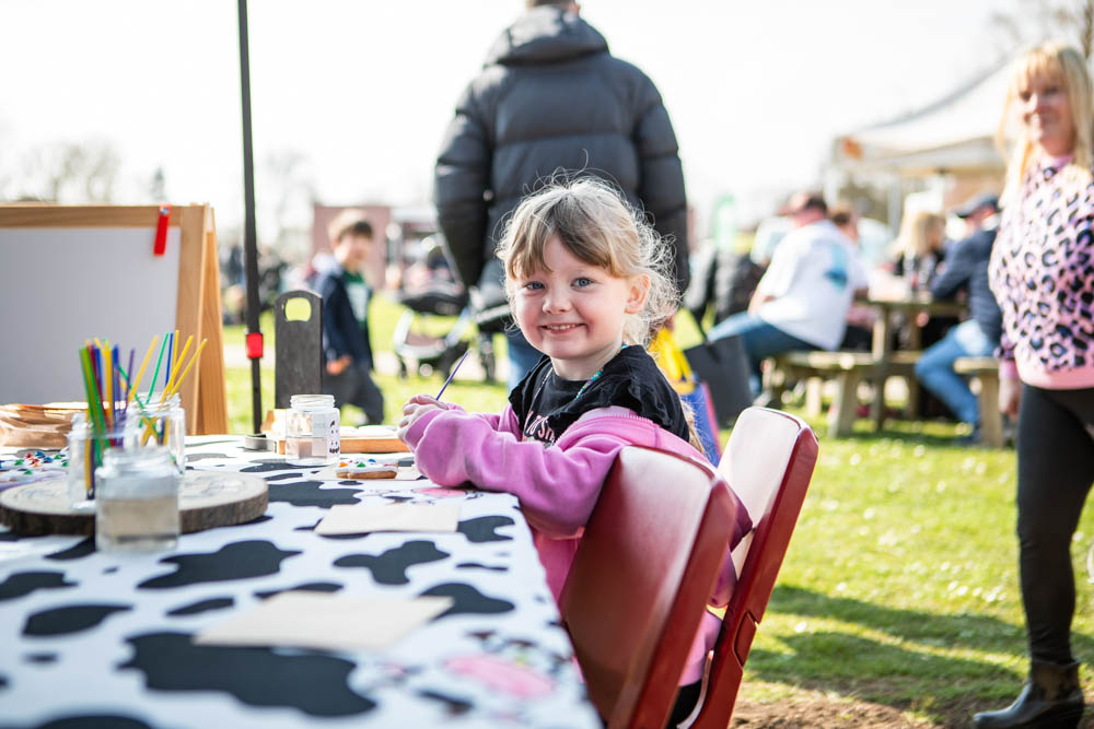 A young girl enjoying arts and crafts at Suffolk New College's spring family fun day, part of the 'lambtastic' event attracting families and children to outdoor activities.