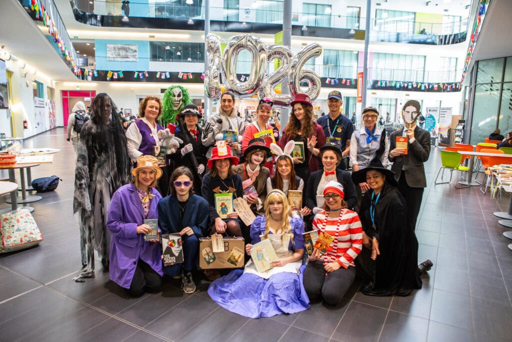 Group of students and staff at Suffolk New College dressed in costumes, celebrating education and skills in a lively indoor setting with decorations and balloons.