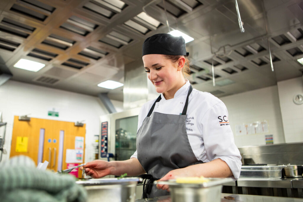Young female restaurant team finalist at Suffolk New College preparing dishes in a professional kitchen, demonstrating culinary skills and teamwork for the competition.