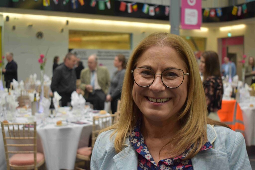 Smiling woman at Suffolk New College's annual dinner celebrating 200 industry partners, with guests and decorated tables in the background.