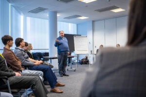 A trainer presenting to students in a classroom setting focused on digital industries, with a whiteboard and attentive learners, highlighting skills development in digital technology.