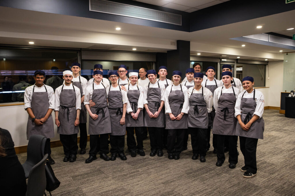Students from Suffolk New College pose in chef uniforms during a special industry dinner event at Ipswich Town Football Club, attended by over 130 guests.