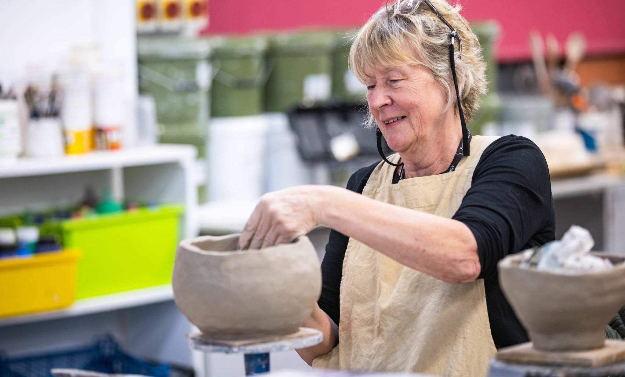 A cheerful woman enjoying pottery making in a classroom setting, demonstrating leisure learning activities at Suffolk New College.