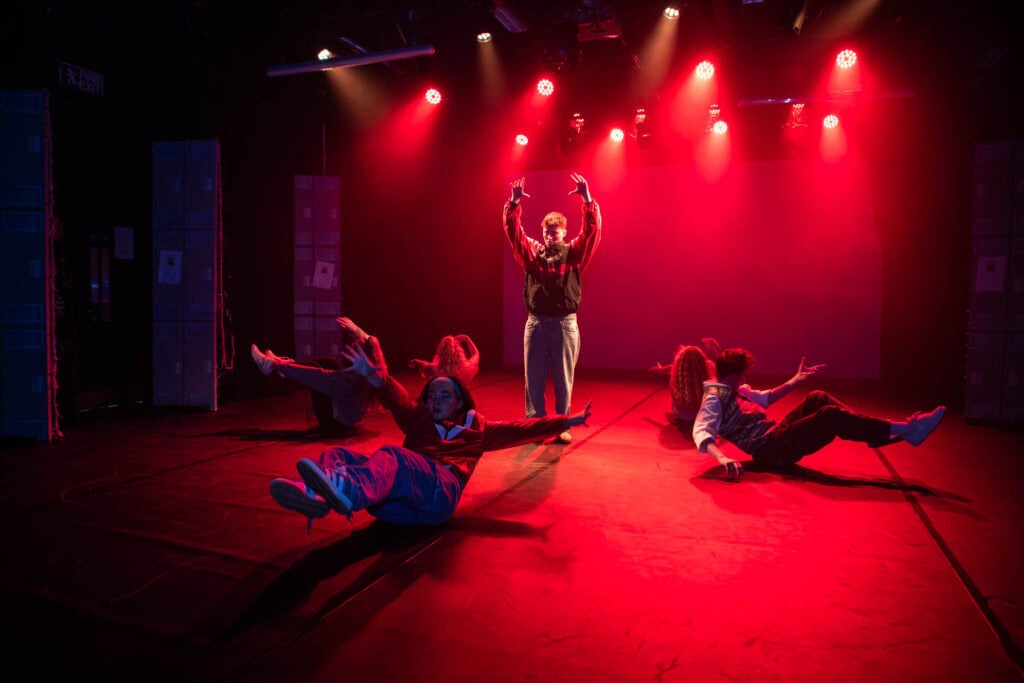 Students at Suffolk New College perform a dynamic dance inspired by Stranger Things on stage, showcasing their production skills and creativity in a vibrant theatre setting.
