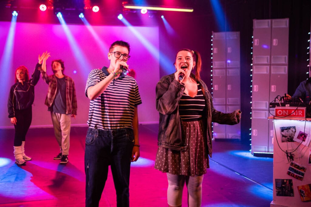 Students at Suffolk New College performing on stage inspired by Stranger Things, showcasing their production skills in a vibrant, colourful theatre setting.